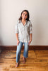 Woman wearing a striped shirt and jeans standing on a wooden floor with a white wall background