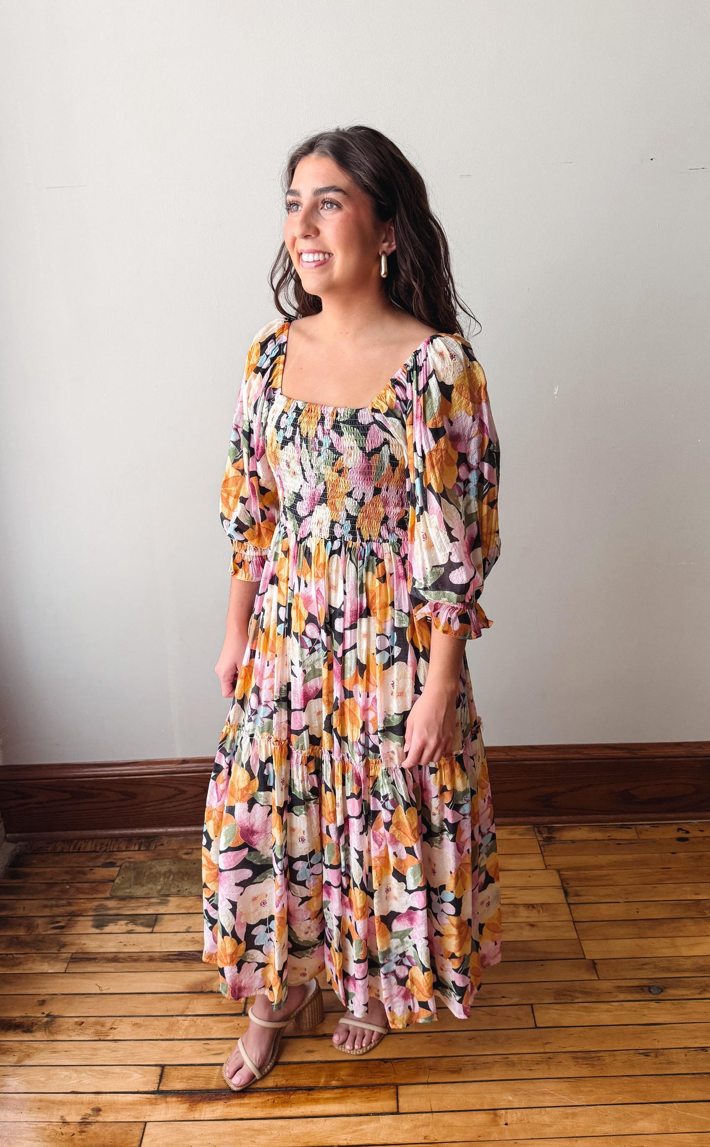 Woman wearing a floral dress standing on a wooden floor with a white wall background