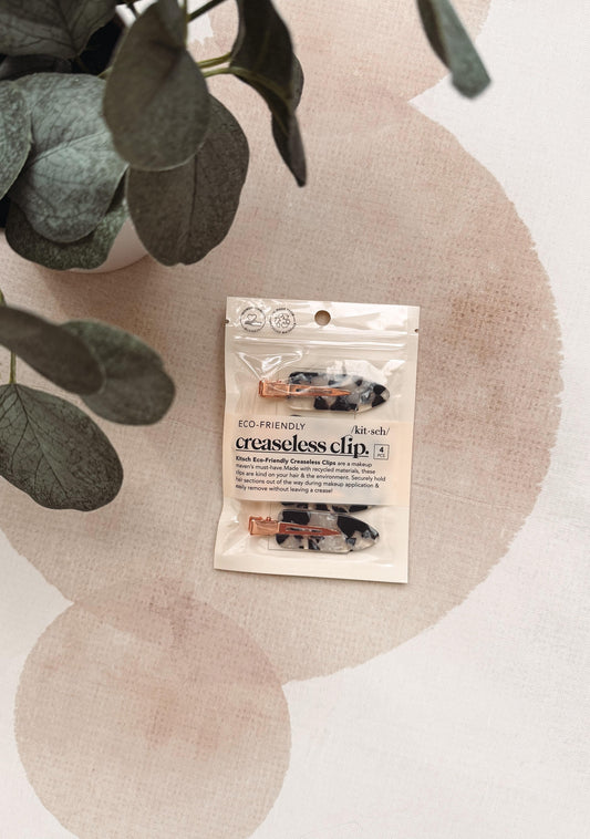 Two small hair clips in a clear resealable pouch labeled 'creaseless clip.' The clips have a glossy finish with a multicolor abstract pattern in black, white, and warm metallic tones.