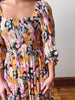 Multicolored patterned dress with smocked bodice and balloon sleeves on a plain background