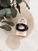 A black flat cloud hair clip attached to a cream-colored Kit-sch retail card, styled on a beige surface with a green plant in the background.