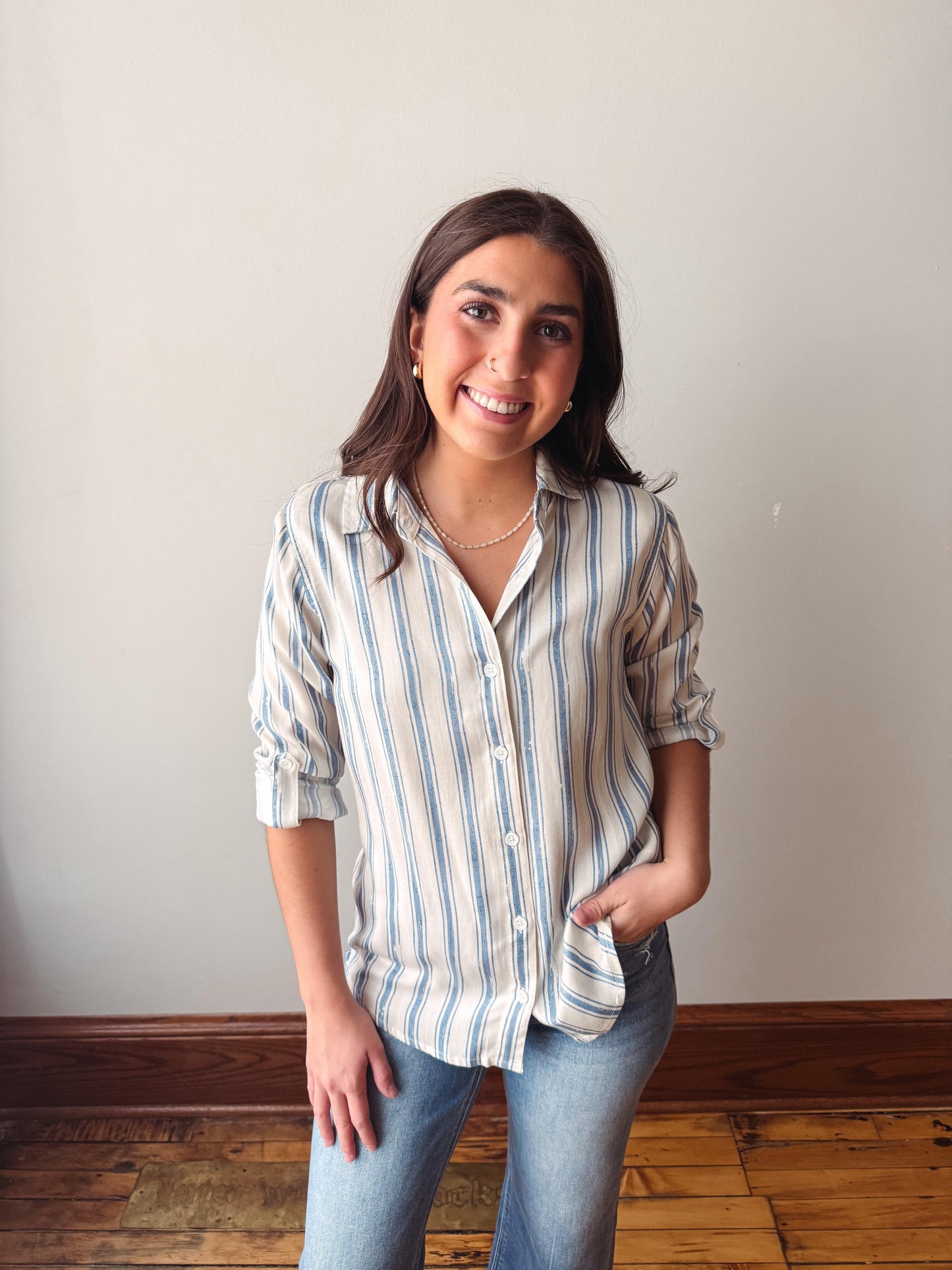 Woman wearing a striped shirt and jeans standing against a plain wall.