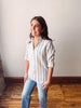 Woman wearing a striped shirt and jeans standing in a room with wooden flooring and white walls.