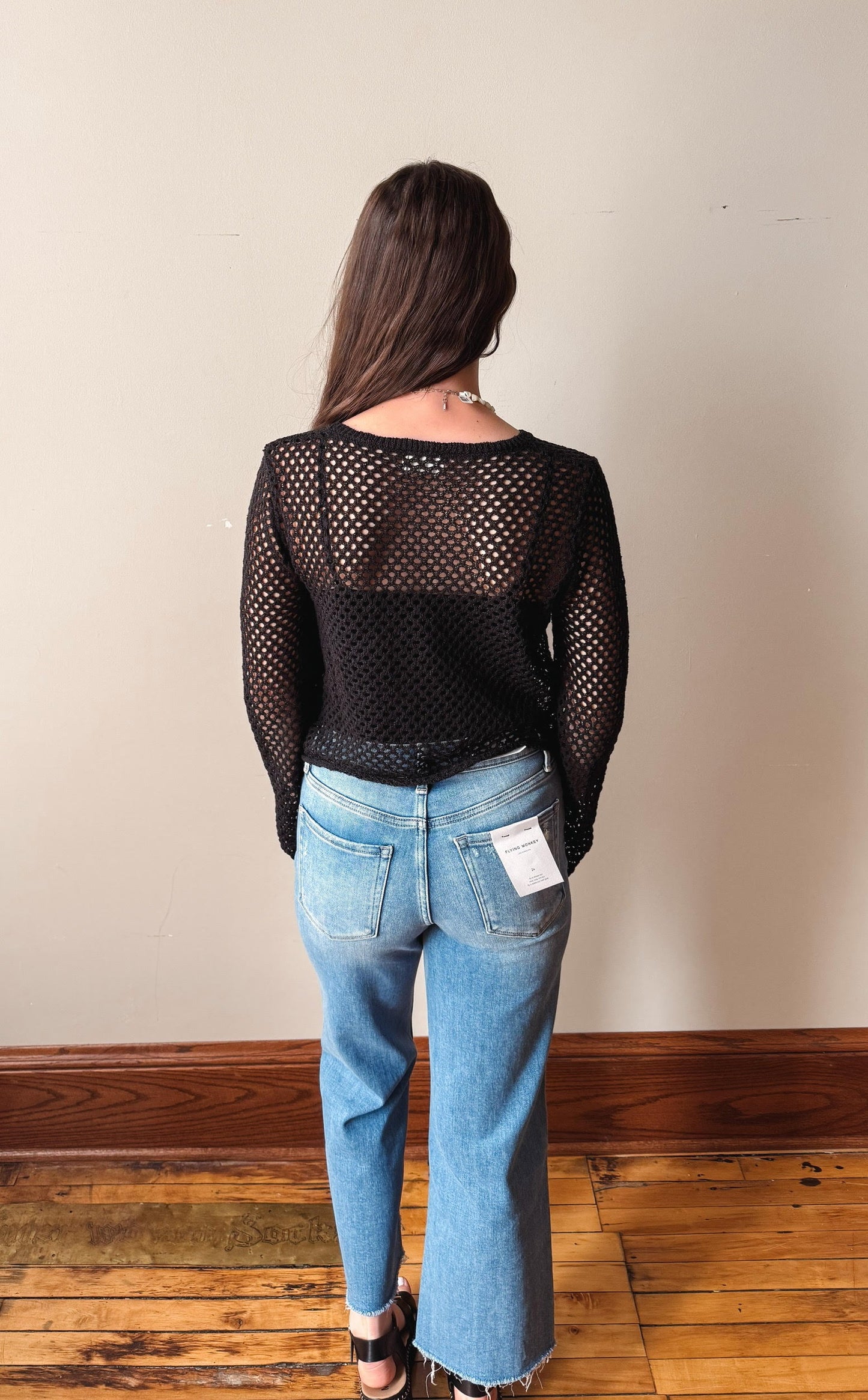 Person wearing a black mesh top and blue jeans with a plain background