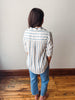 Person wearing a striped shirt and jeans standing on a wooden floor against a white wall.