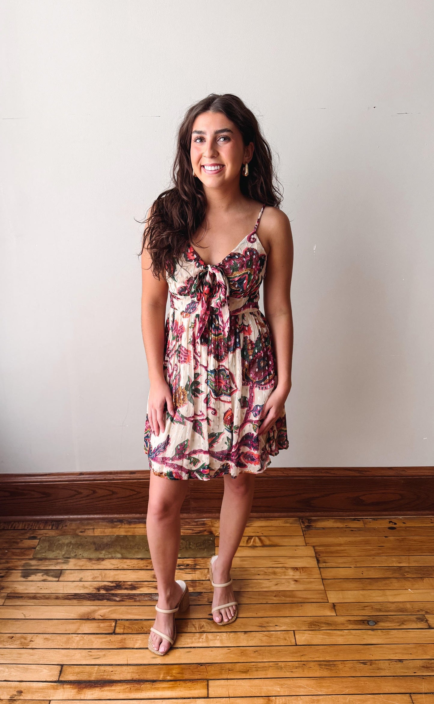 Woman wearing a floral dress standing on a wooden floor with a white wall background