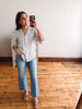 Woman taking a mirror selfie wearing a striped shirt and jeans in a room with wooden flooring.