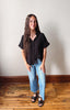 Woman wearing a black shirt and blue jeans standing on a wooden floor with a white wall background