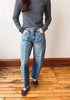 A person wearing a navy and gray striped long-sleeve shirt and light-wash blue jeans, standing on a wooden floor against a plain wall.