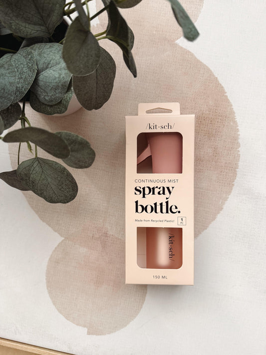 Kit sch spray bottle packaging box in a soft blush pink color, displayed on a textured beige surface with a green plant leaf in the foreground.
