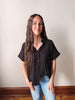 Woman wearing a black blouse and blue jeans against a plain wall.