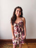 Woman wearing a floral dress standing against a plain wall.