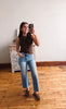Woman taking a mirror selfie wearing a brown top and light blue jeans in a room with wooden flooring.