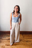 Woman wearing a light blue tank top and beige wide-leg pants standing on a wooden floor.