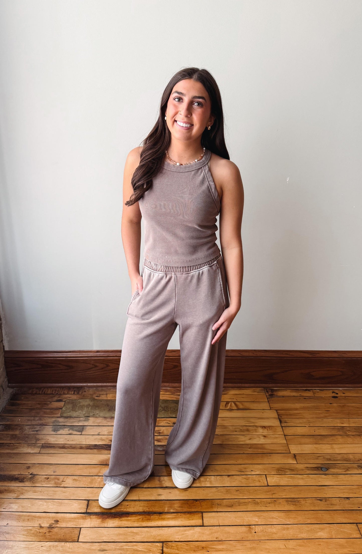 Woman wearing a gray sleeveless top and wide-leg pants standing on a wooden floor.