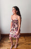 Woman wearing a floral dress standing on a wooden floor against a white wall.
