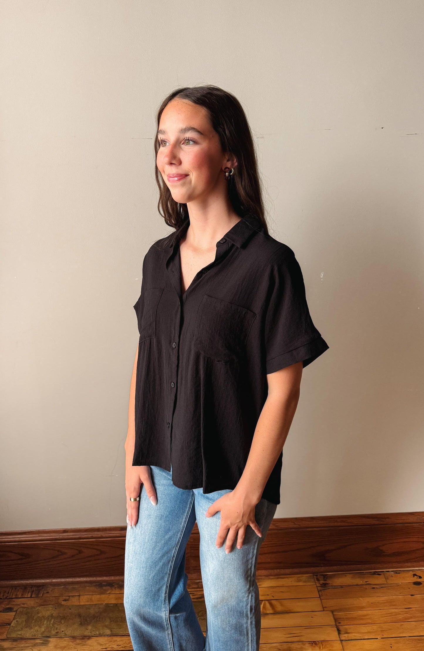 Woman wearing a black shirt and blue jeans standing against a plain wall.