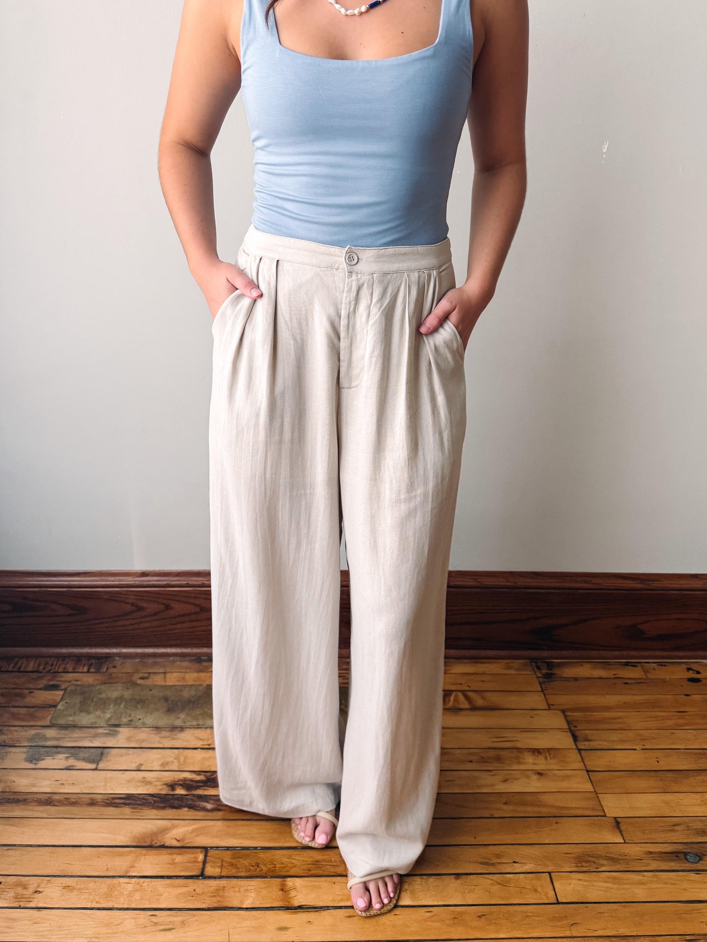 Person wearing a light blue tank top and beige wide-leg pants on a wooden floor.