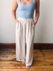 Person wearing a light blue tank top and beige wide-leg pants on a wooden floor.