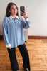 A woman taking a mirror selfie wearing a light blue and white vertically striped button-down shirt with a white collar and cuffs, paired with black wide-leg pants.