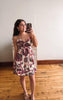 Woman taking a mirror selfie wearing a floral dress in a room with wooden flooring.