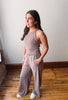 Woman wearing a gray sleeveless top and pants standing in a room with wooden flooring.