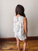 Woman wearing a floral romper standing against a plain wall.