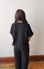 Person wearing a black outfit standing against a plain white wall.