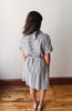 Woman wearing a checkered dress standing on a wooden floor with a white wall background