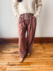 A person wearing loose, wide-leg dusty rose drawstring pants with a cream ribbed knit sweater, standing on a wooden floor against a plain wall.