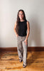 Woman wearing a black top and patterned pants standing against a plain wall.