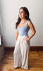 Woman wearing a light blue tank top and beige wide-leg pants standing in a room with wooden flooring.