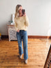 Woman taking a mirror selfie wearing a yellow cardigan and blue jeans in a room with wooden flooring.