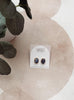 A pair of oval stud earrings with dark blue and white marbled inlay and gold-tone edges, displayed on a white backing card labeled Urban Jewelry, styled on a textured beige surface with a plant leaf in the corner.