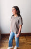 Woman wearing a gray t-shirt and blue jeans standing against a white wall.