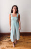 Woman wearing a light blue striped dress standing on a wooden floor with a white wall background