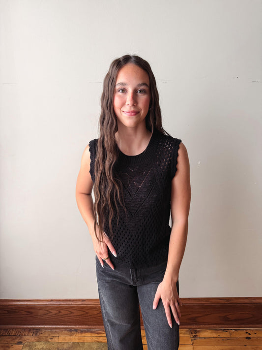 Woman wearing a black sleeveless top with a textured pattern against a plain wall.