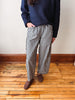 A person wearing black and white gingham wide-leg trousers, a navy blue sweater, and brown suede loafers, standing on a wooden floor against a white wall.
