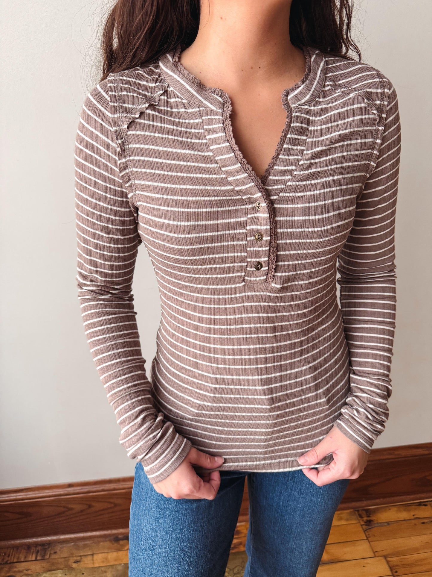 A woman wearing a brown and white striped long-sleeve henley top with ruffle trim at the collar and button placket, paired with blue jeans.