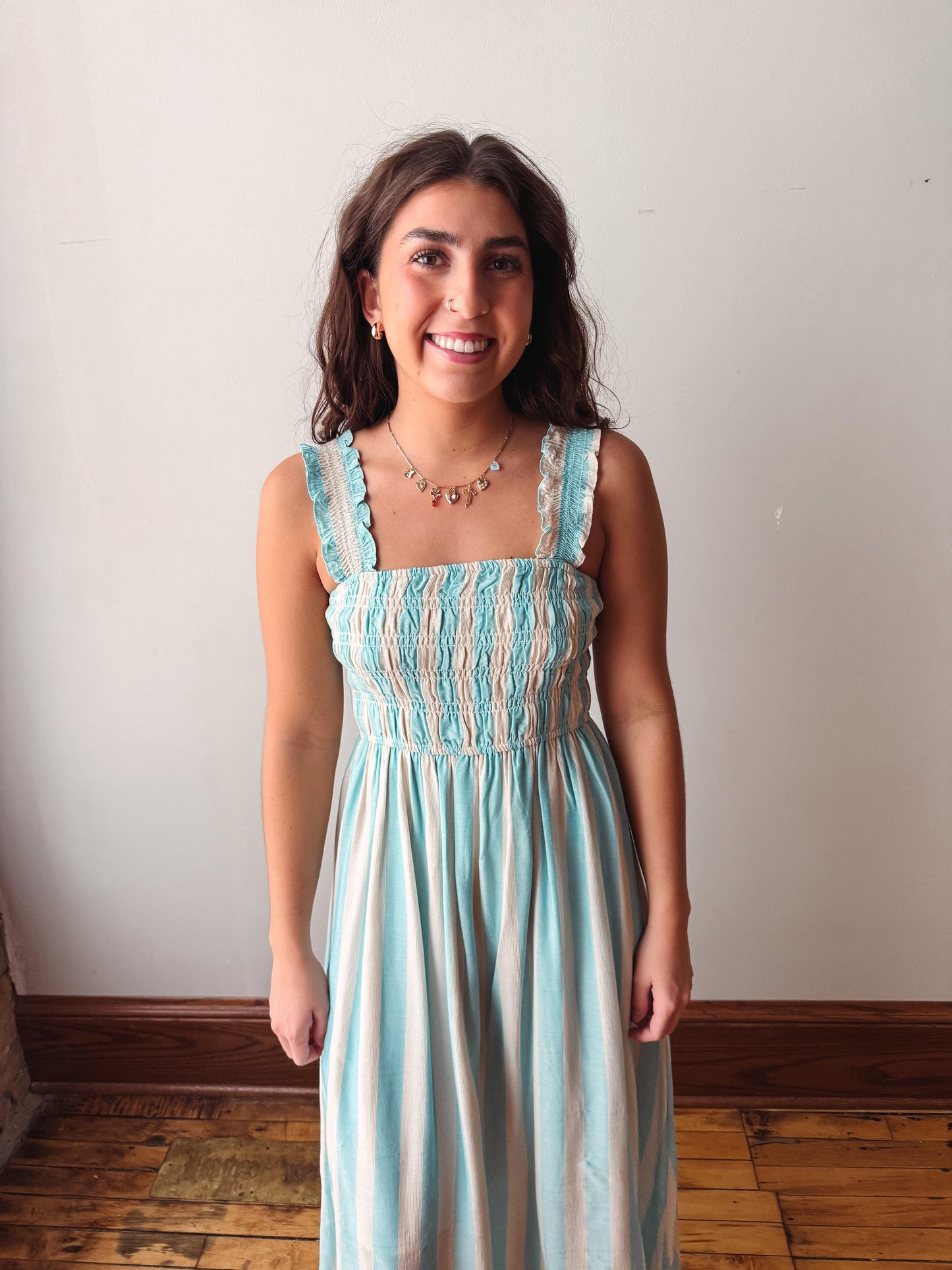 Woman wearing a light blue and white striped dress standing against a plain wall.
