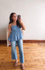 Woman taking a mirror selfie wearing a blue top and jeans in a room with wooden flooring.