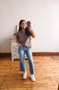 Woman taking a mirror selfie wearing a gray t-shirt, blue jeans, and white sneakers in a room with wooden flooring and a decorative cabinet.