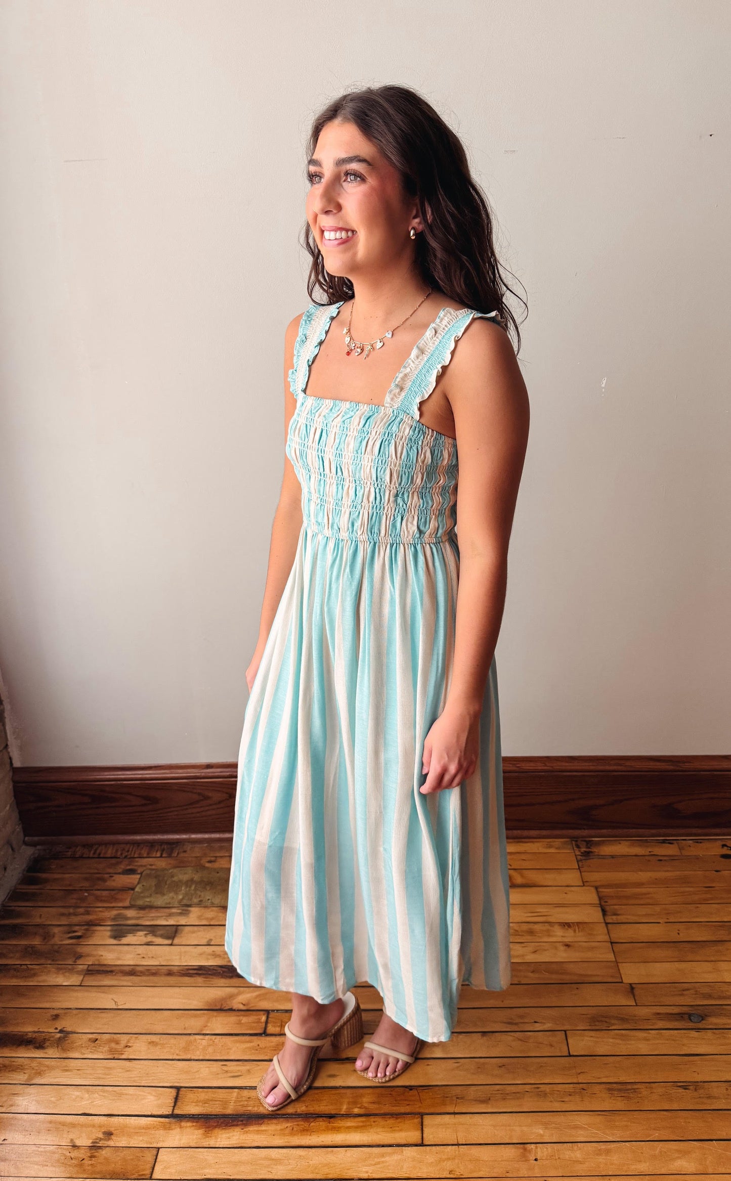 Woman wearing a light blue and white striped dress standing on a wooden floor.