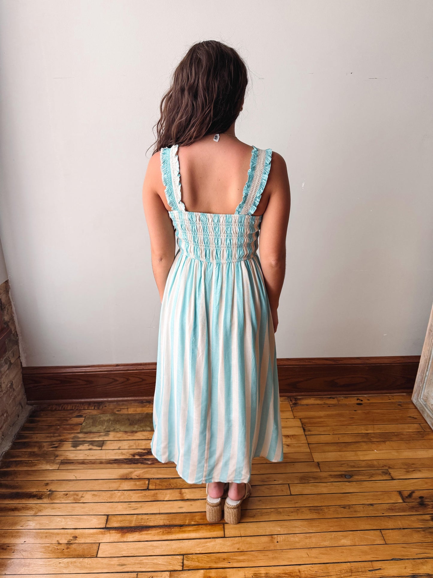 Woman wearing a light blue striped dress standing on a wooden floor with a white wall background
