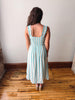 Woman wearing a light blue striped dress standing on a wooden floor with a white wall background