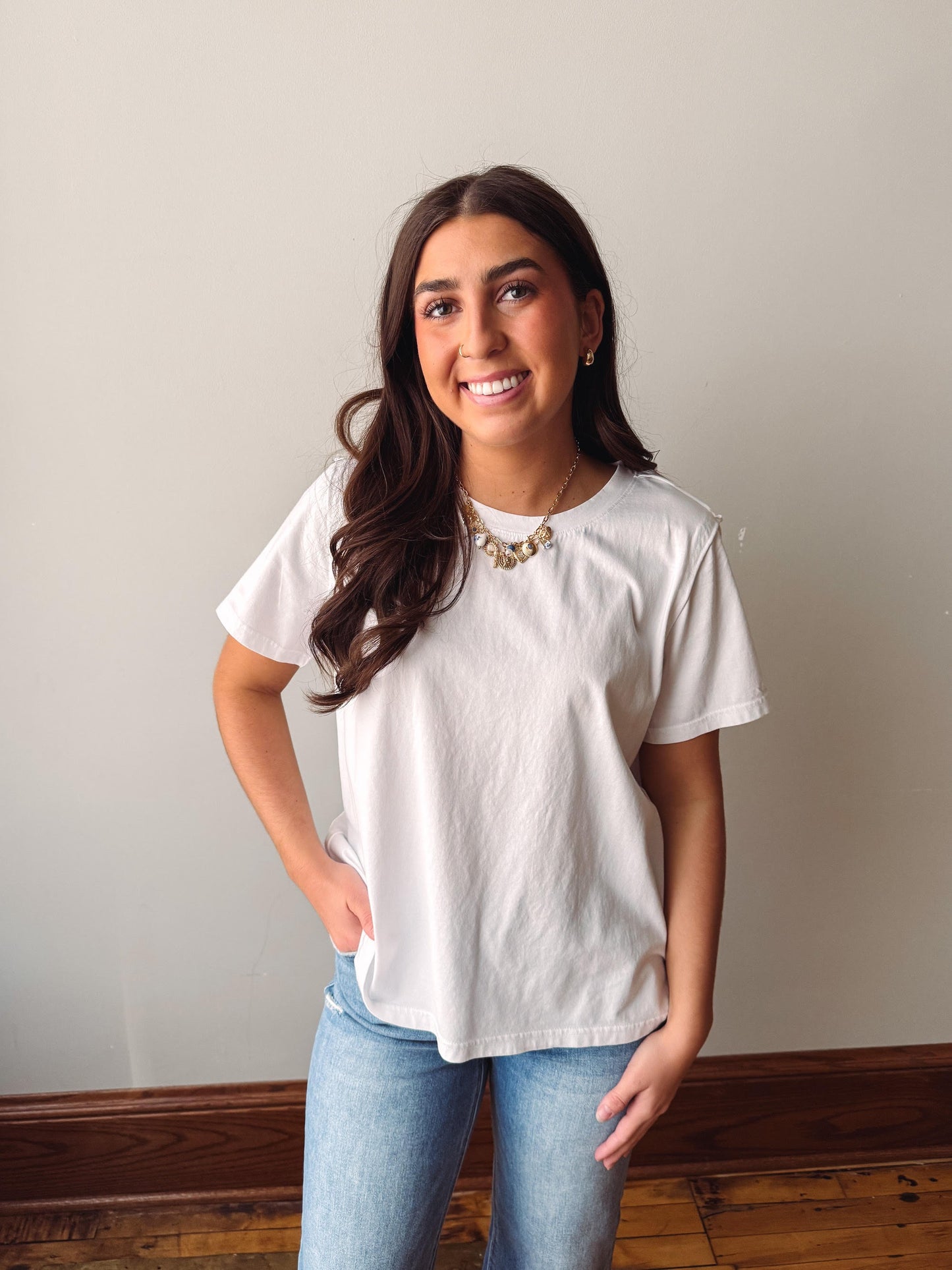 Woman wearing a white t-shirt and blue jeans standing against a plain wall.