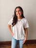 Woman wearing a white t-shirt and blue jeans standing against a plain wall.
