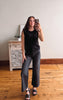 Woman taking a mirror selfie wearing a black top and gray pants in a room with wooden flooring and a white dresser.