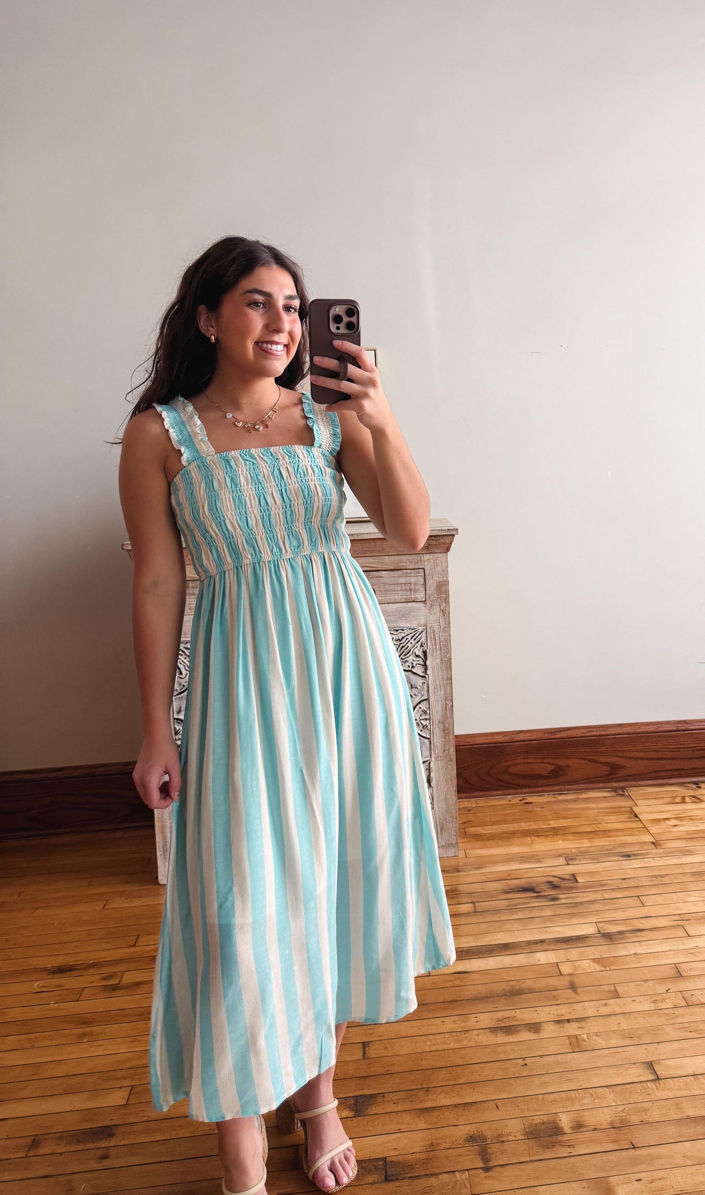 Woman taking a mirror selfie wearing a striped dress in a room with wooden flooring.