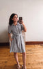 Woman taking a mirror selfie wearing a checkered dress in a room with wooden flooring.